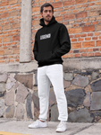 Man with hands in pocket in super driven  standing in front of a brick wall wearing super driven legend black motivational eco-friendly hoodie